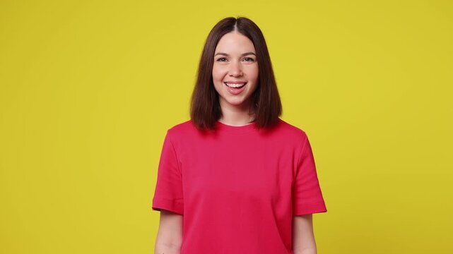 Smiling friendly fun charming young Caucasian woman she wearing pink t-shirt casual clothes looking camera wink eye blink isolated on plain yellow color background studio portrait. Lifestyle concept