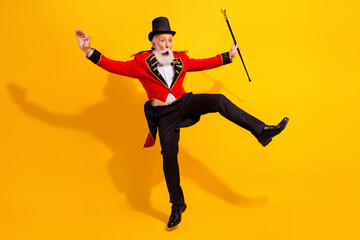 Energetic elderly circus magician performs a lively kick and shows off tricks in a bright yellow...