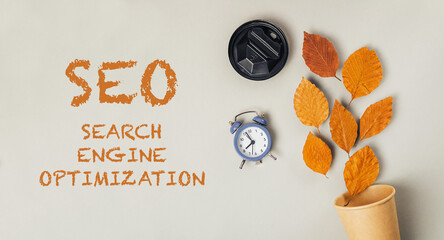 SEO concept with autumn leaves, clock, and coffee cup on a neutral background for digital marketing