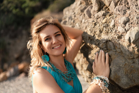 Woman portrait smiling, enjoying summer vacation on rocky beach. Natural beauty with turquoise jewelry, confident and happy expression. - Powered by Adobe