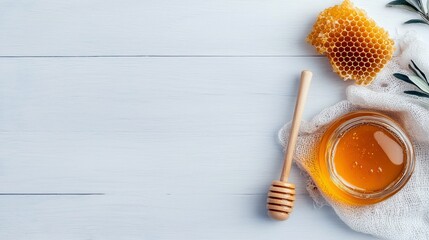 A top-down shot of a jar of honey, a honeycomb, and a honey dipper on a white wooden surface. The scene is lit with natural light.