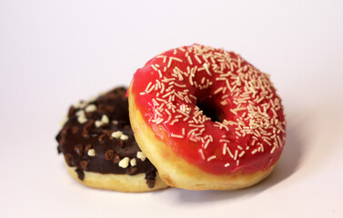 Two glazed donuts — one with red icing and white sprinkles, another with chocolate glaze and nut sprinkles — on a clean minimal light background. Bright, appetizing food stock photo for commercial use