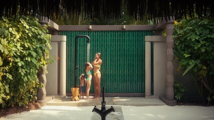 A mother and her children enjoy a refreshing outdoor shower together at a luxurious island resort. They are having a wonderful family vacation in a tropical paradise villa.