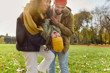 Happy family play among autumn leaves in park. Parents lift a giggling child upside down, sharing laughter, enjoying nature and outdoors. Playful love, joyful family bonding outdoors.