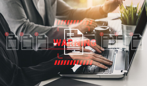 Focus on hands typing on a laptop with a warning symbol showing potential cybersecurity risks in a modern office environment, emphasizing document safety. Gantry