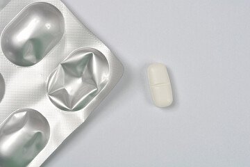 A single white, oval pill lies beside a partially used silver blister pack with crumpled empty...