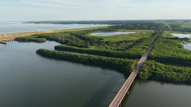 Aerial view of a long bridge crossing a river surrounded by green land