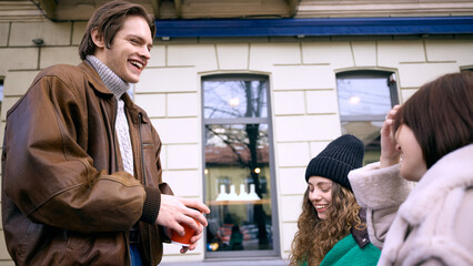 Friends laughing and enjoying hot coffee together outside city cafe in winter. Concept of youth lifestyle marketing, outdoor beverage campaigns and authentic real-people communication visuals