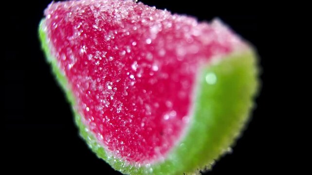 Watermelon Slice Marmalade Candy rotating on black. Macro shot of red and green triangular gummy with sugar coating. Summer fruit flavored dessert.