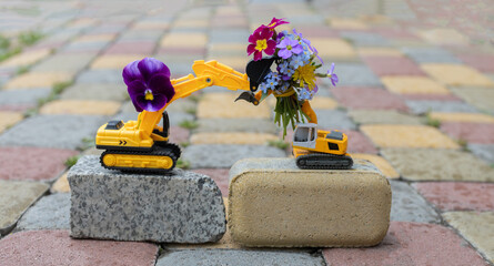 bouquet of small flowers on an excavator bucket. Two toy excavators. buckets of machines are...