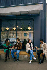 Group spending time together with hot drinks outside city cafe in winter weather. Concept of...
