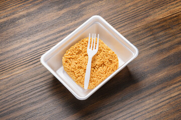 Dried instant noodles and white disposable fork in plastic plate