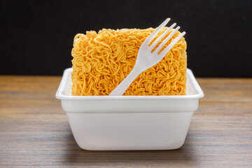 Dried instant noodles and white disposable fork in plastic plate