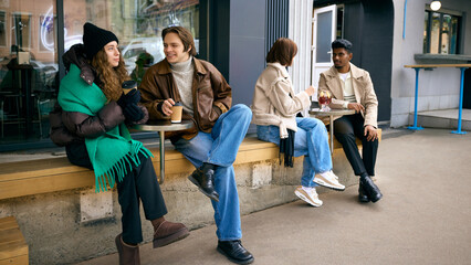 Young women enjoying hot coffee and autumn conversation on outdoor bench. Concept of seasonal...