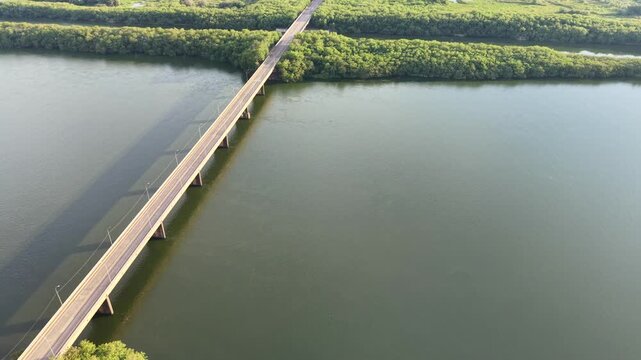Aerial view of a long bridge crossing a wide river with green treesides
