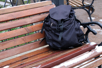 Black backpack left on park bench in winter