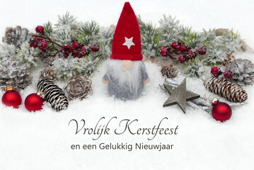Kerstkaart: Kerstmanfiguur met kerstversiering en dennentakken in de sneeuw, met de Nederlandse...