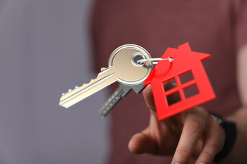 Person holding house keys with a red house keychain, representing homeownership, new home purchase, or real estate.