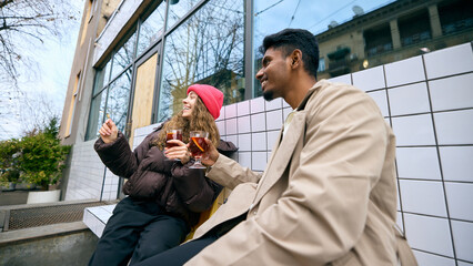 Obraz premium Young people enjoying warm beverages outside modern building. Concept of winter event ambience, mobile service takeaway culture, financial wellness lifestyle, and relaxed social interaction.