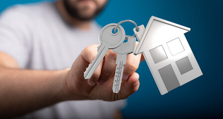 Close-up shot of a man holding house keys with a house keychain, representing homeownership, real...
