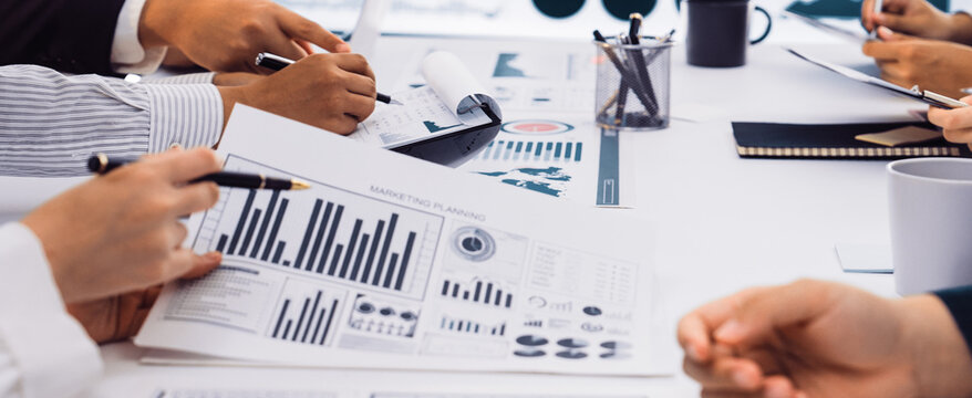 A diverse business team engages in a collaborative meeting focused on data analysis and strategic planning, surrounded by charts, graphs, and interactive reports. SACTR - Powered by Adobe