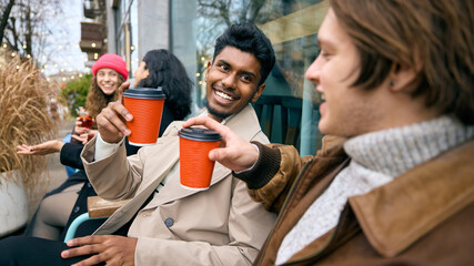 Young men toasting takeaway drinks during cold season hangout. Concept of urban lifestyle, delivery...
