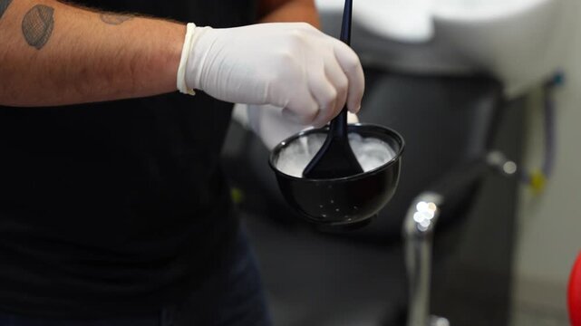 Close-up of hairdresser&rsquo;s gloved hand using a spatula to mix bleaching powder and oxidant in a bowl