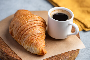 Tasty flaky french croissant and cup of espresso coffee on wooden serving board