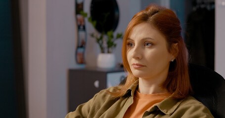 Professional redhead freelancer working remotely from home office, sitting on chair while intensely focusing on computer screen and processing business task