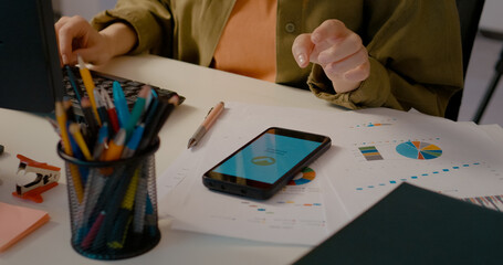 Woman types on her computer in a home office, then checks her phone to confirm if the online payment has been accepted during her workday.