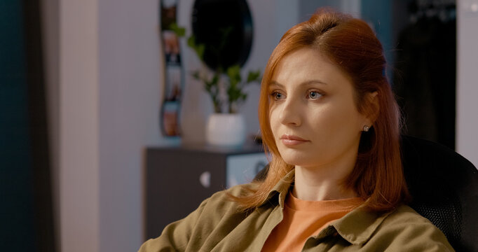 Professional redhead freelancer working remotely from home office, sitting on chair while intensely focusing on computer screen and processing business task