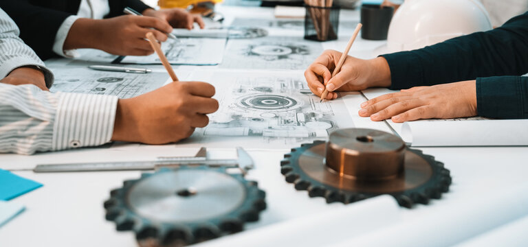A team of engineers and designers collaborates on technical drawings while surrounded by gears and tools in a modern office. The image captures the essence of teamwork and innovation. SACTR