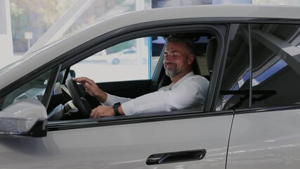 Man customer male buyer client wear white sit in car hold steering wheel shirt chooses auto wants to buy new automobile in car showroom vehicle salon dealership store motor show indoor. Sales concept