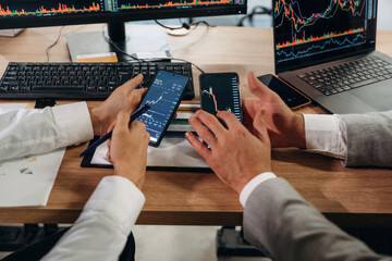 Fototapeta premium Comparing the data. Close up view of hands of business men that are working with stock market exchange
