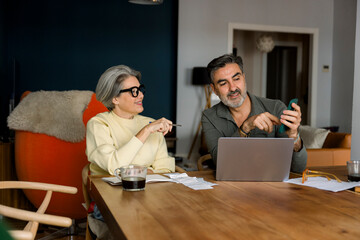 Senior couple budgeting finances using laptop and smartphone