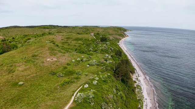 Aerial drone footage of grassy coastal cliffs and shoreline with green fields and wildflowers along the sea.