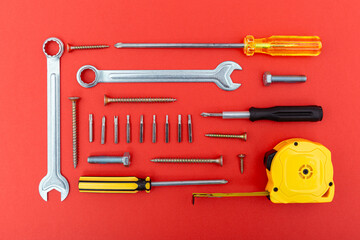 Various tools including screwdrivers, wrench, bolts and tape measure on red background. Concept of...