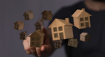 Conceptual image of hand touching floating wooden houses, representing property investment, real estate, and the dream of homeownership.