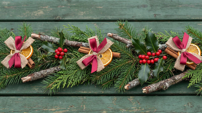 Rustic christmas garland with evergreen branches, dried orange slices, cinnamon sticks, holly leaves and red berry ribbon decorations