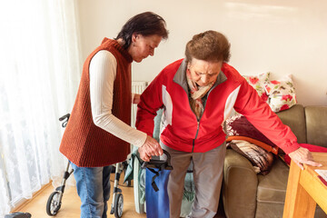 Senior woman exercising with resistance band supported by caregiver for strength, mobility and fall prevention at home