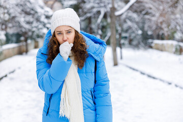 Woman in winter coat coughs on snowy street