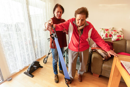 Senior woman exercising with resistance band supported by caregiver for strength, mobility and fall prevention at home - Powered by Adobe