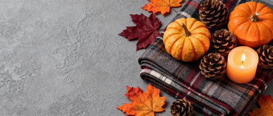 cozy autumn arrangement with pumpkins, pine cones, plaid blanket, candle and colorful leaves on textured gray background