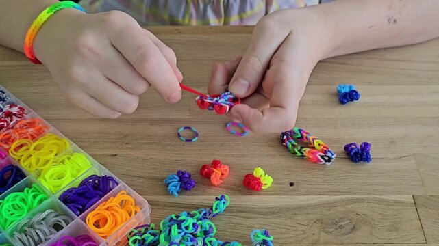 Colorful rubber band crafts shown by children making bracelets at a wooden table