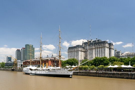 Vista de la hist&oacute;rica Fragata Sarmiento anclada en Puerto Madero, con el imponente Edificio Libertador y rascacielos modernos de fondo bajo un cielo azul.