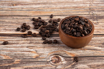 Coffee beans in a wooden cup against a wooden table background.