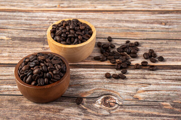 Coffee beans in a wooden cup against a wooden table background.