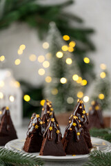 Chocolate brownie Christmas tree with chocolate glaze and sugar sprinkles on top on a white plate. Christmas or New Year festive dessert. Copy space.