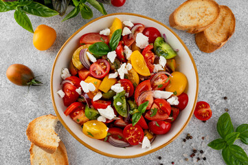 A salad of farm fresh multi-colored tomatoes, red onion, fresh basil and feta cheese in a bowl. Summer salad. Top view.