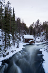 winter river flowing by old wooden mill in snowy finnish forest in National park Oulanka